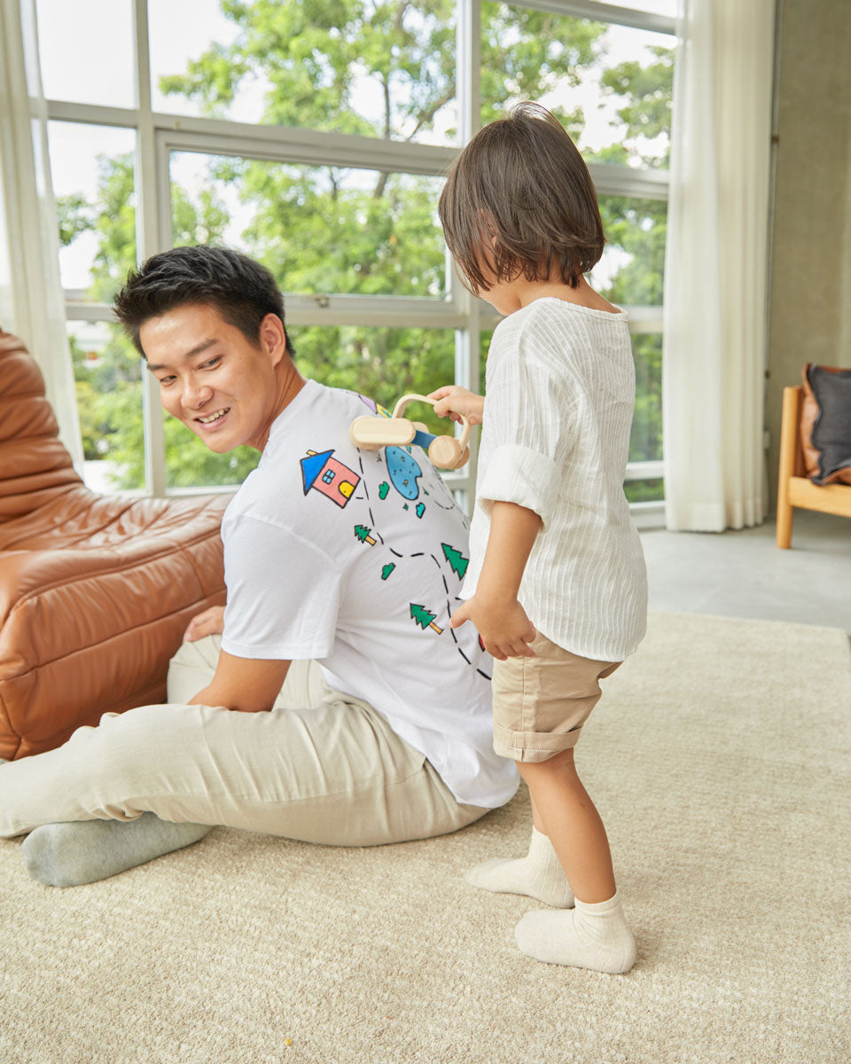 Man sat down on the floor with a child pushing the PlanToys wooden push along sensory massage roller across his back