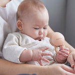 Close up of a baby in an adult's arms playing with the PlanToys plastic-free wooden shake rattle baby toy. 