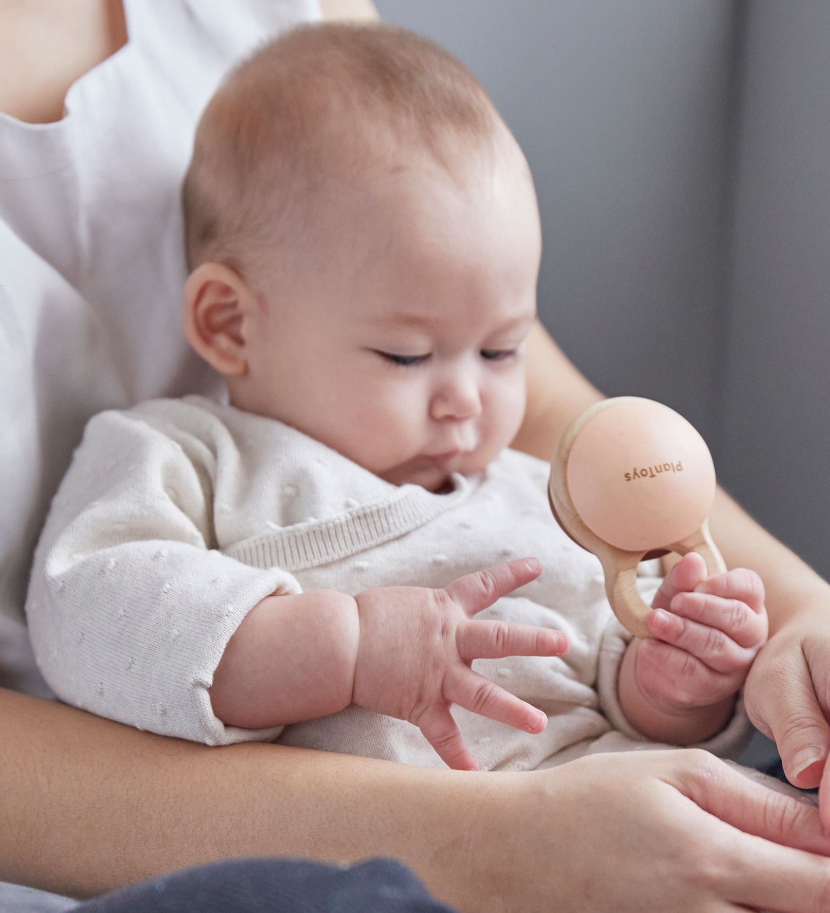 Close up of a baby in an adult's arms playing with the PlanToys plastic-free wooden shake rattle baby toy. 