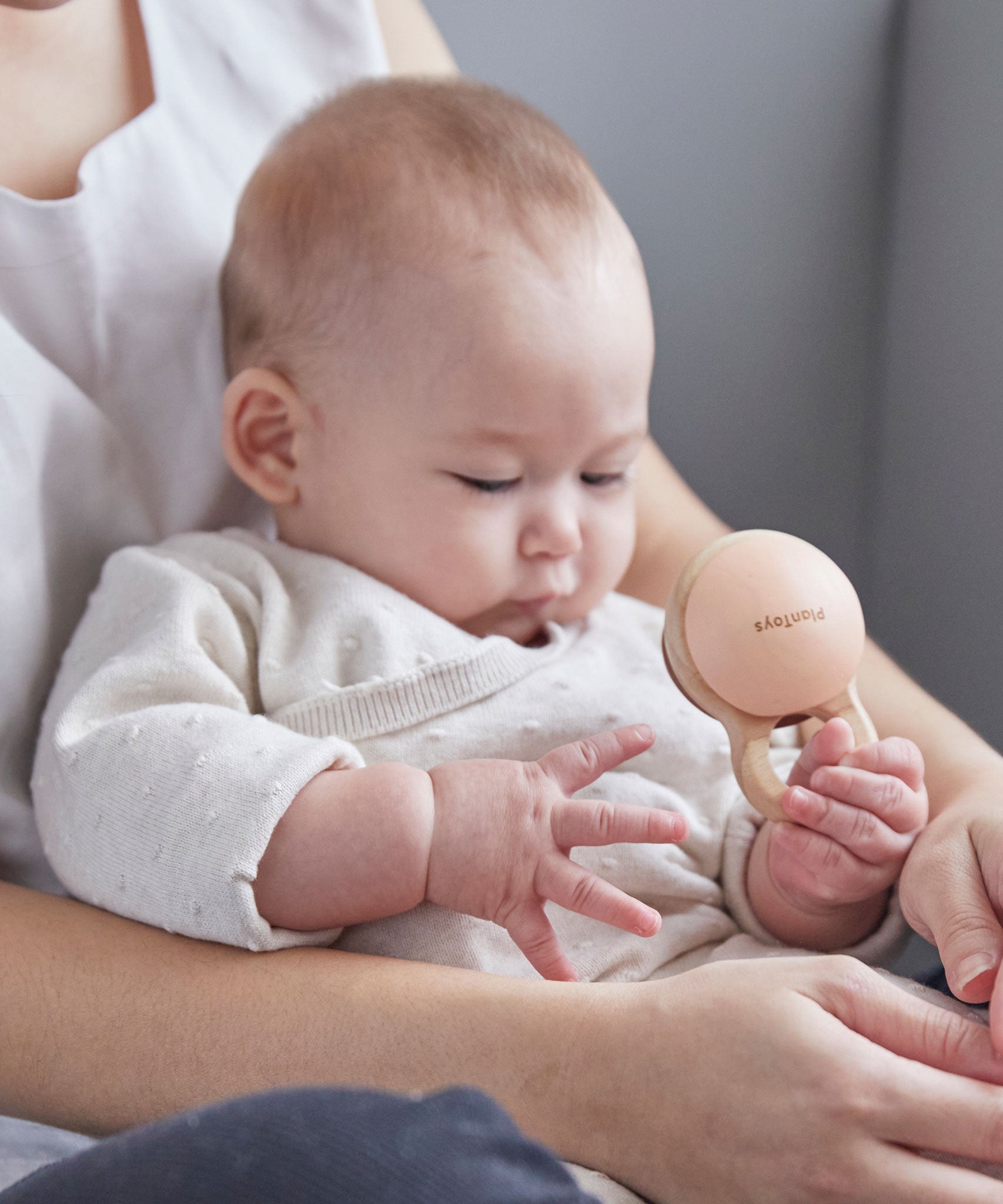 Close up of a baby in an adult's arms playing with the PlanToys plastic-free wooden shake rattle baby toy. 