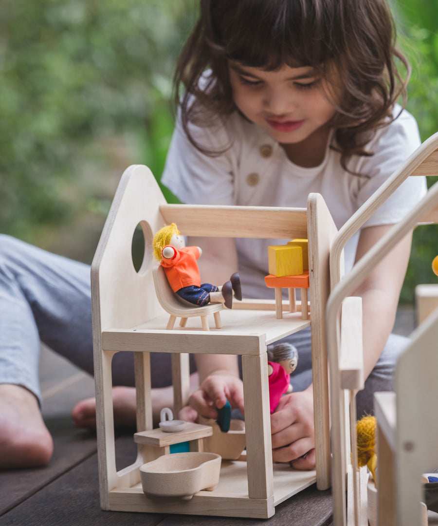 A child playing with the PlanToys Slide N Go Dolls' House, the pieces of furniture can be seen placed inside with PlanToys dollies. 