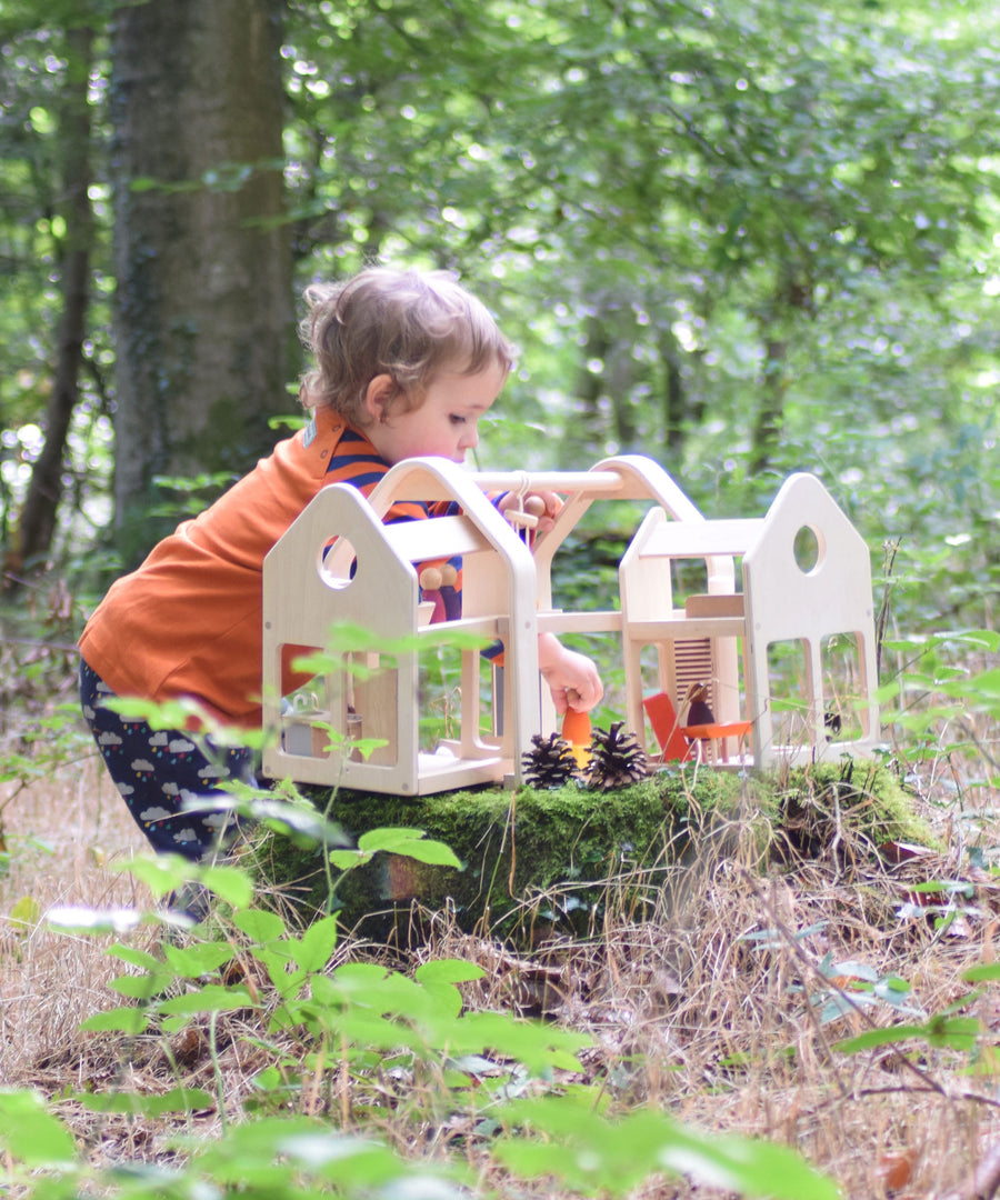 A child playing with the PlanToys Slide N Go Dolls' House placed on a moss covered tree stump in the forest. 