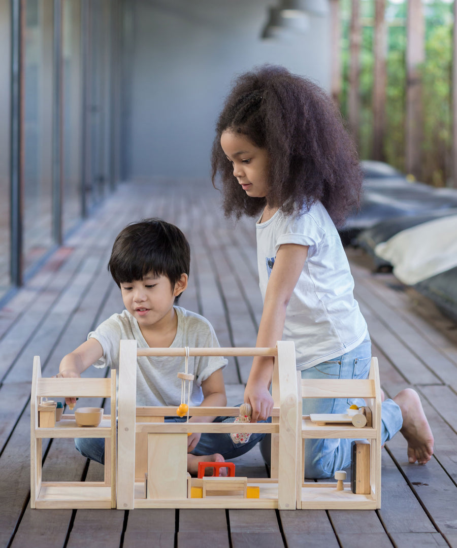 Two children playing with the PlanToys Slide N Go Dolls' House that has been placed on wooden flooring.