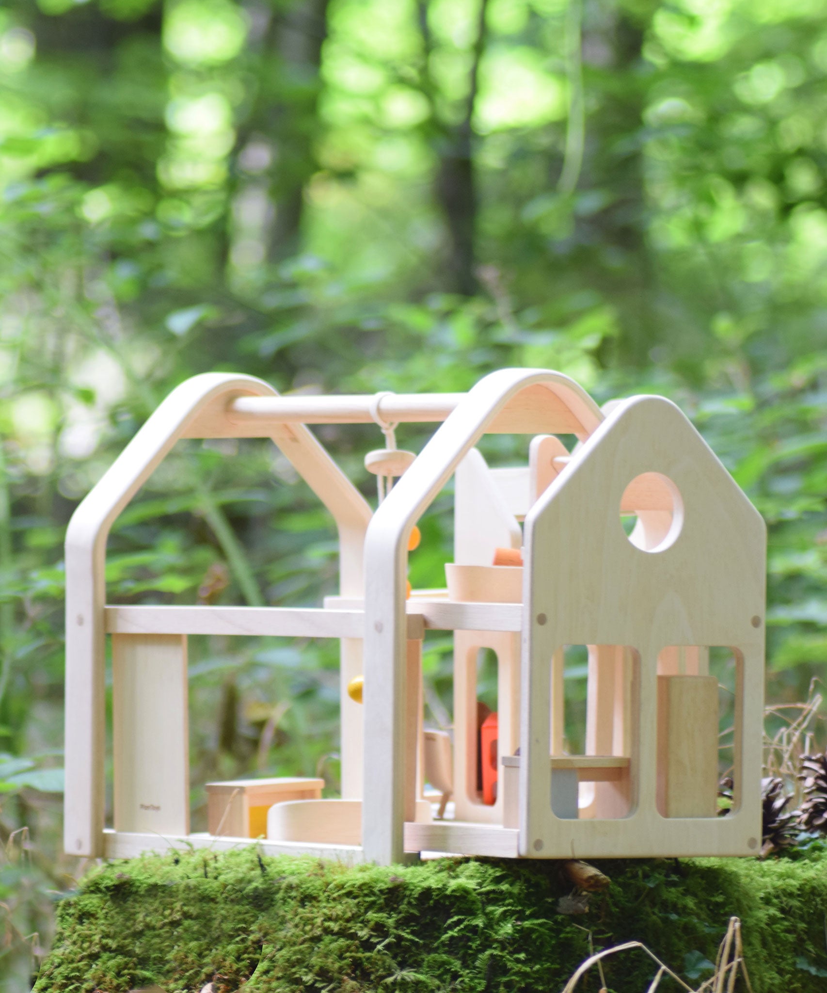 The PlanToys Slide N Go Dolls' House placed on a moss covered tree stump in the forest. 