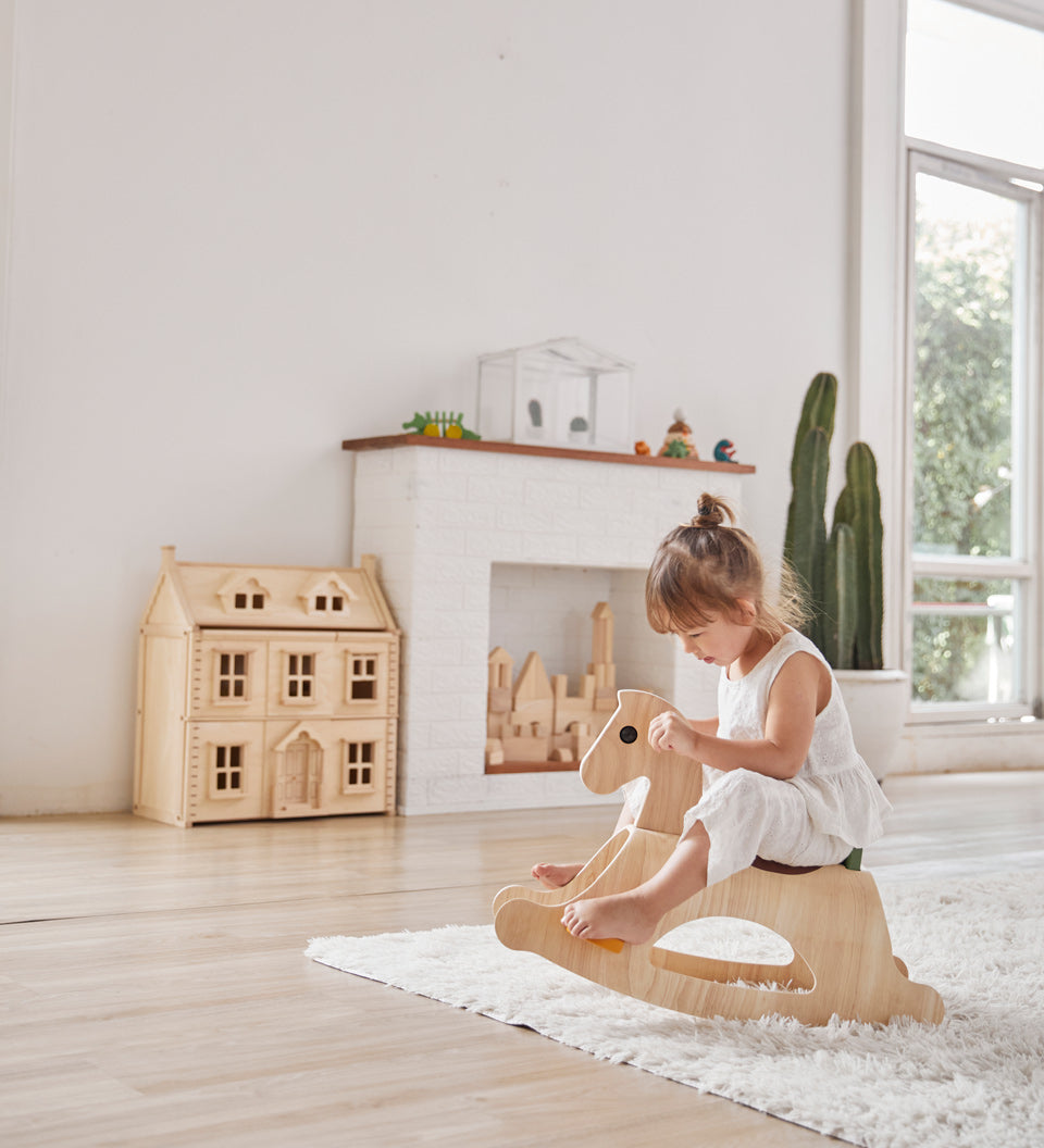 Young girl sat on the PlanToys children's palomino rocking horse on a white fluffy rug in a light playroom