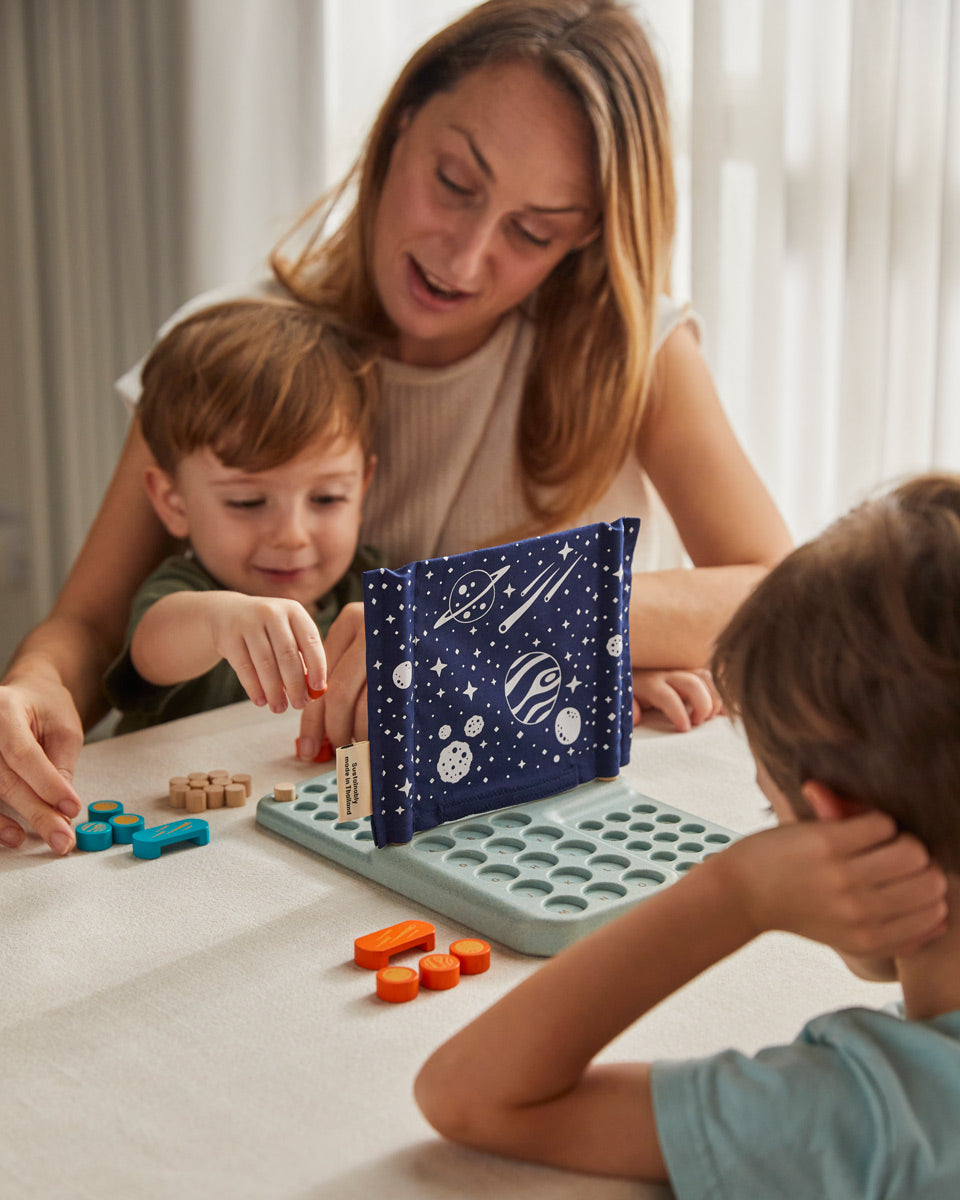 Children with an adult sitting by a table playing with the PlanToys Guess My Planet Game. 