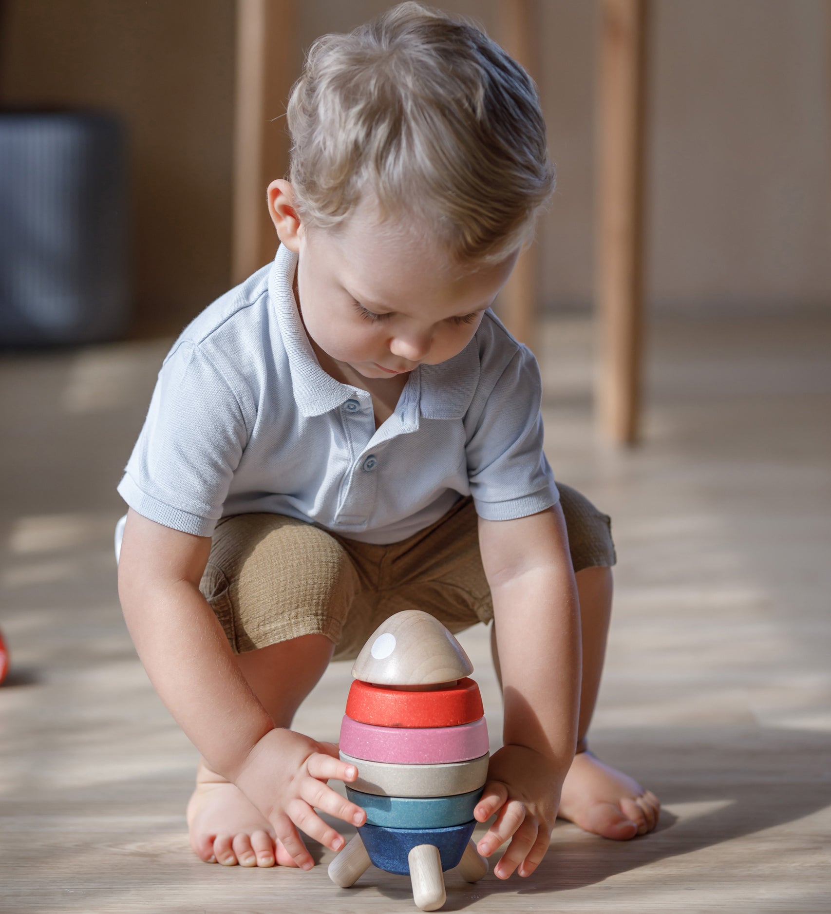 A child crouching down playing with the PlanToys orchard colour way Stacking Rocket Baby Toy.