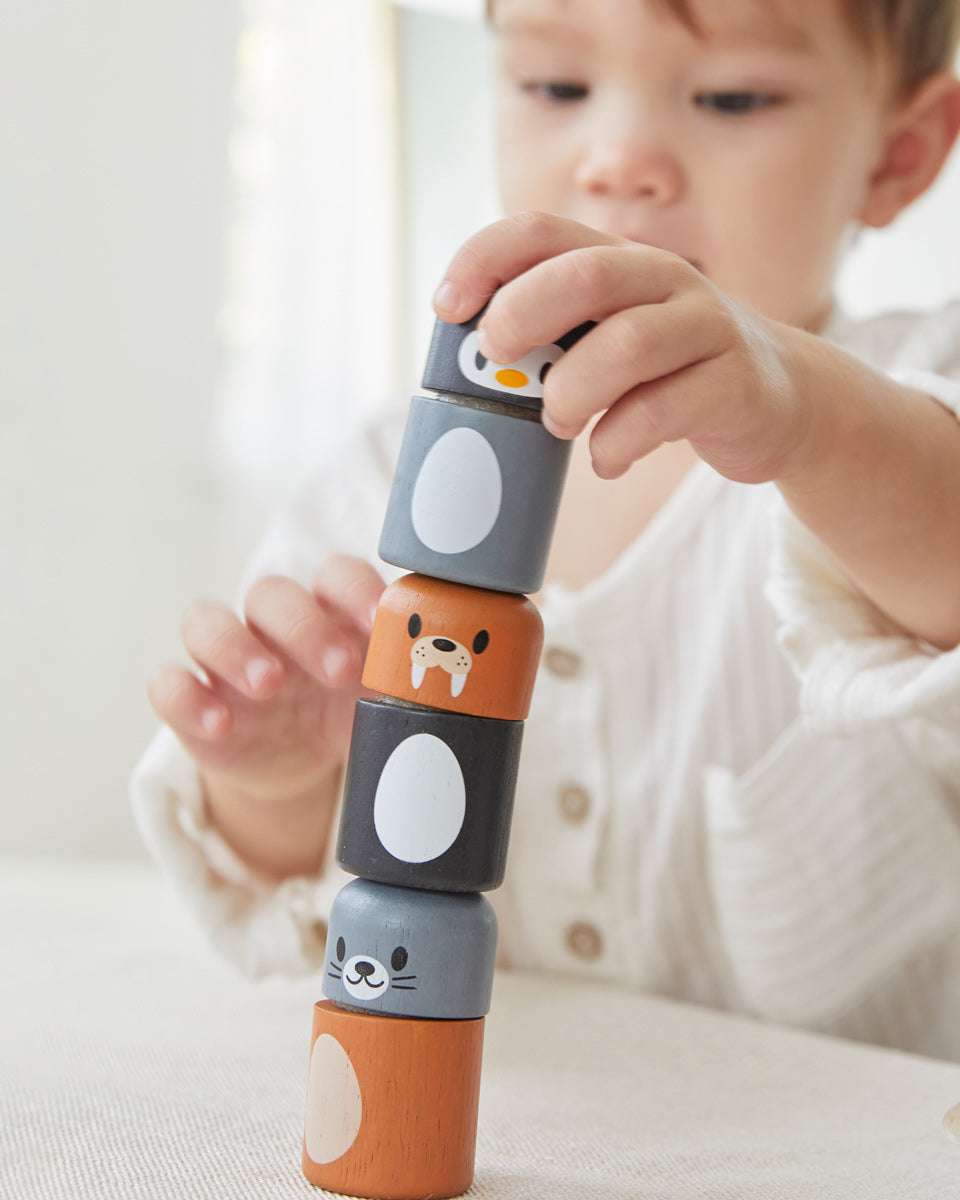 Close up of young boy making a tower with the PlanToys arctic animals matching figures on a white table.