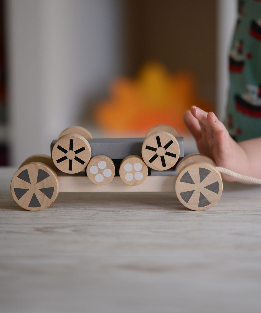 The Plan Toys Stacking Wheels toy, a child's hand can be seen on the side pushing the wheels.