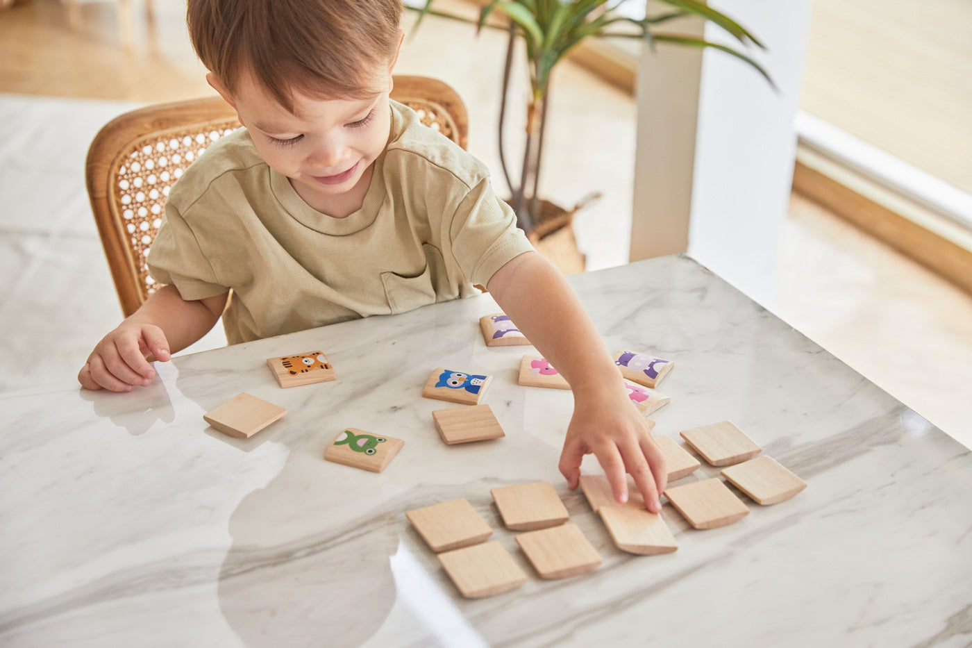 A young boy sat at a white marble table playing with the PlanToys wooden animal memory game. 