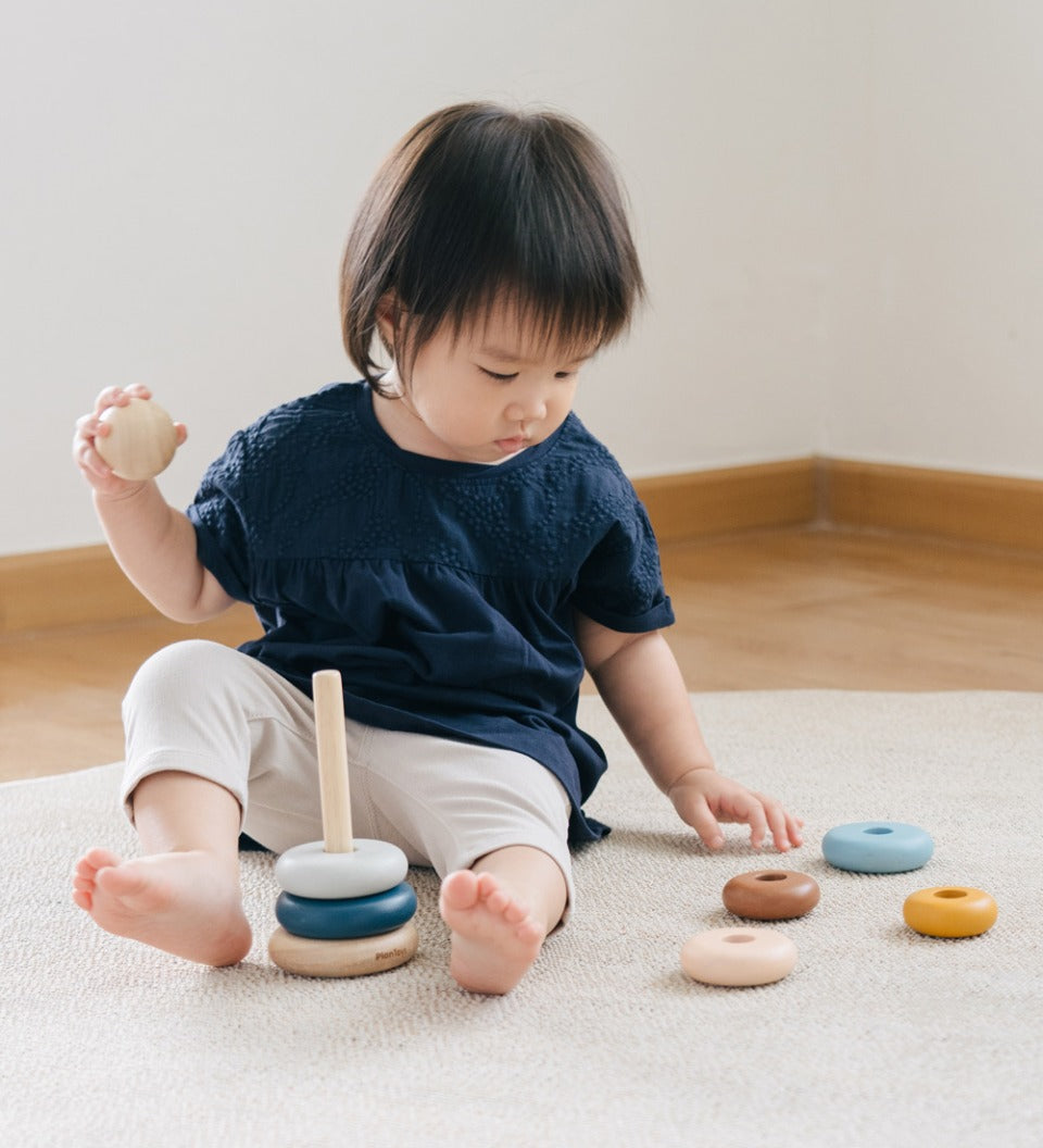 Child sat on a grey carpet playing with the PlanToys plastic-free wooden stacking orchard rings