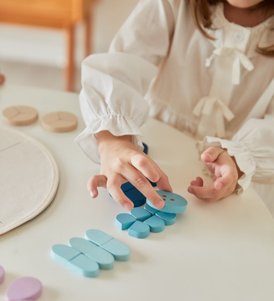 Young girl lining up blue pieces from the PlanToys Waldorf mandala set on a white table