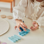 Young girl lining up blue pieces from the PlanToys Waldorf mandala set on a white table