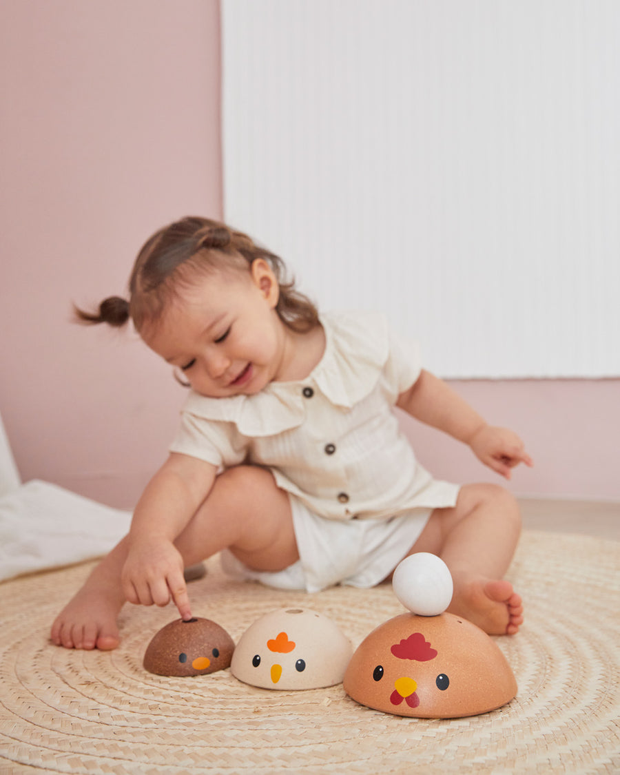 Girl leaning over to place a toy egg on top of the PlanToys stacking wooden bowls