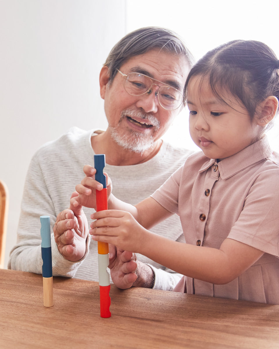 Young girl and man sat at a wooden table stacking blocks from the PlanToys plastic-free logs puzzle