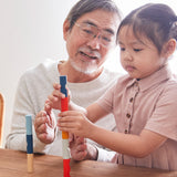 Young girl and man sat at a wooden table stacking blocks from the PlanToys plastic-free logs puzzle