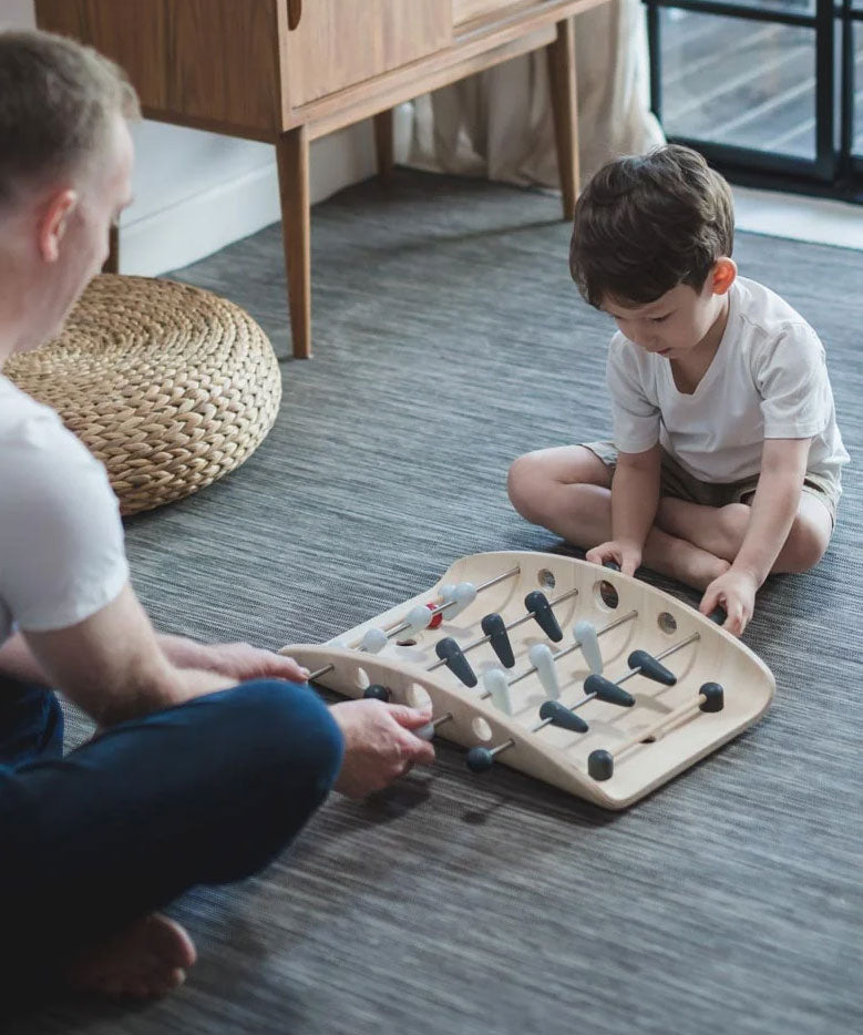 A child and adult playing with the PlanToys wooden soccer game. 