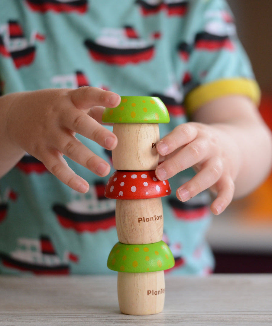 A child stacking three PlanToys Mushroom Kaleidoscopes on top of each other. 