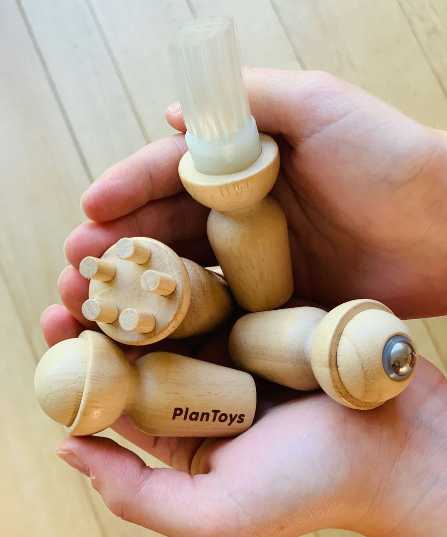 The four tools from the PlanToys Touch & Guess Sensory Game being held in a person's hands. 