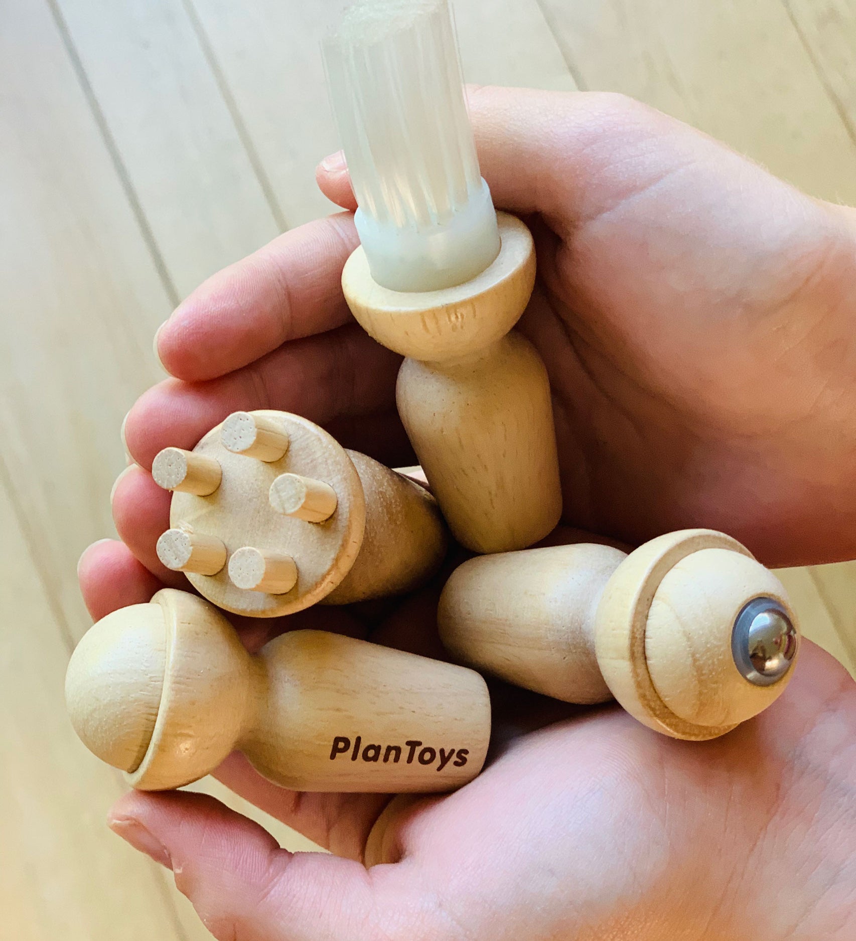 The four tools from the PlanToys Touch & Guess Sensory Game being held in a person's hands. 