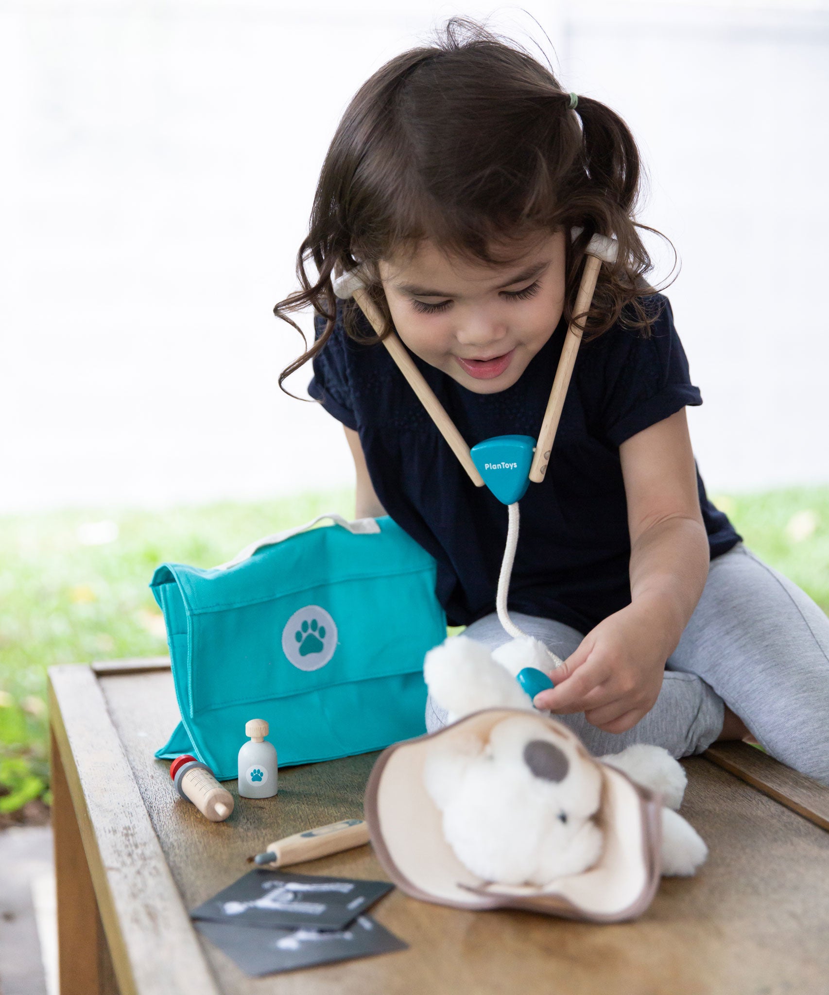 A child playing with the Plan Toys Play Vet Set, they have a teddy as their patient. 