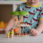 The PlanToys PlanWorld Tree House being played with by a child. The child's hand can be seen holding onto the little wooden ladder. 