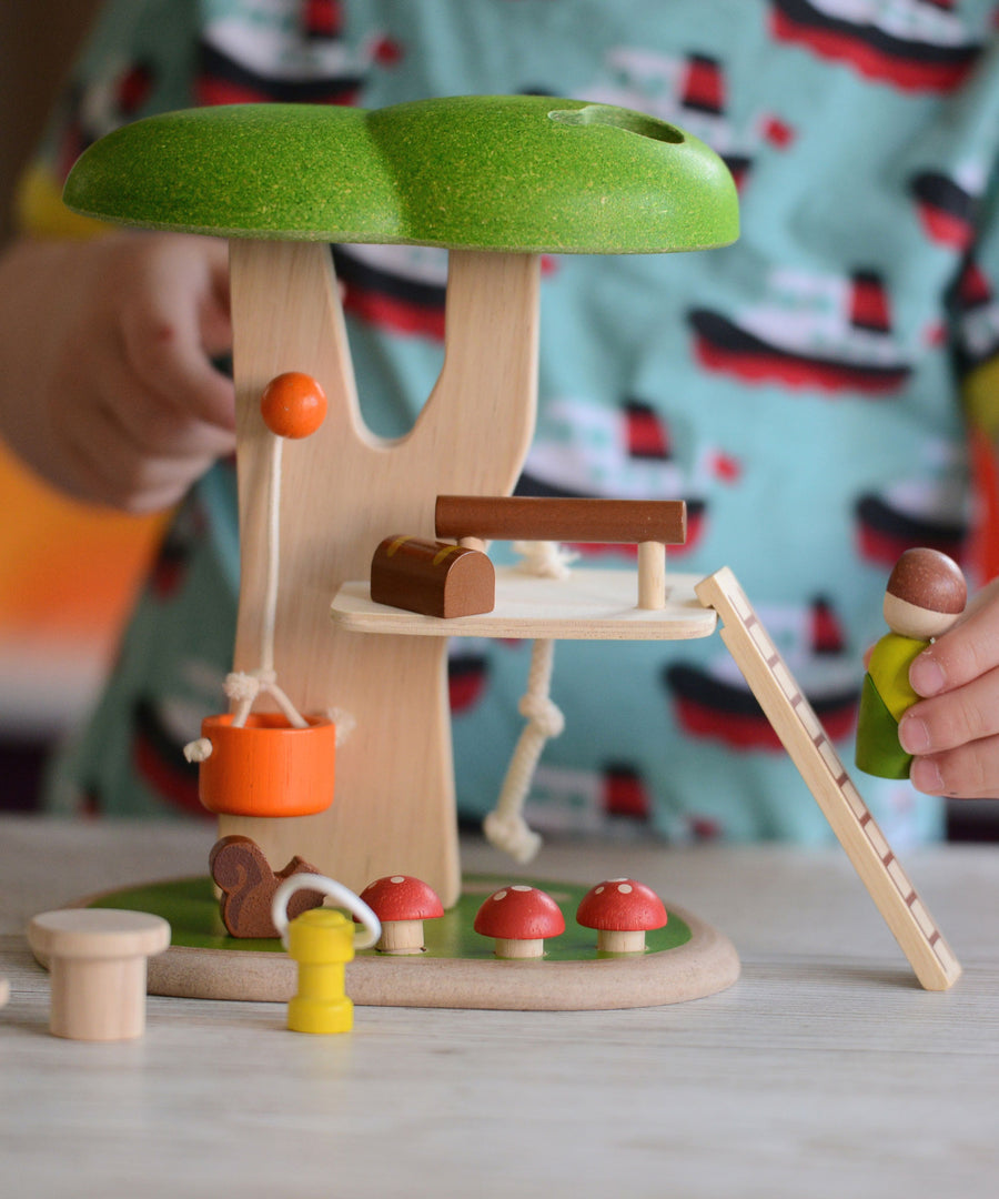 A close up of the PlanToys PlanWorld Tree House being played with by a child. The child's hand can be seen holding onto the little wooden doll figure. 