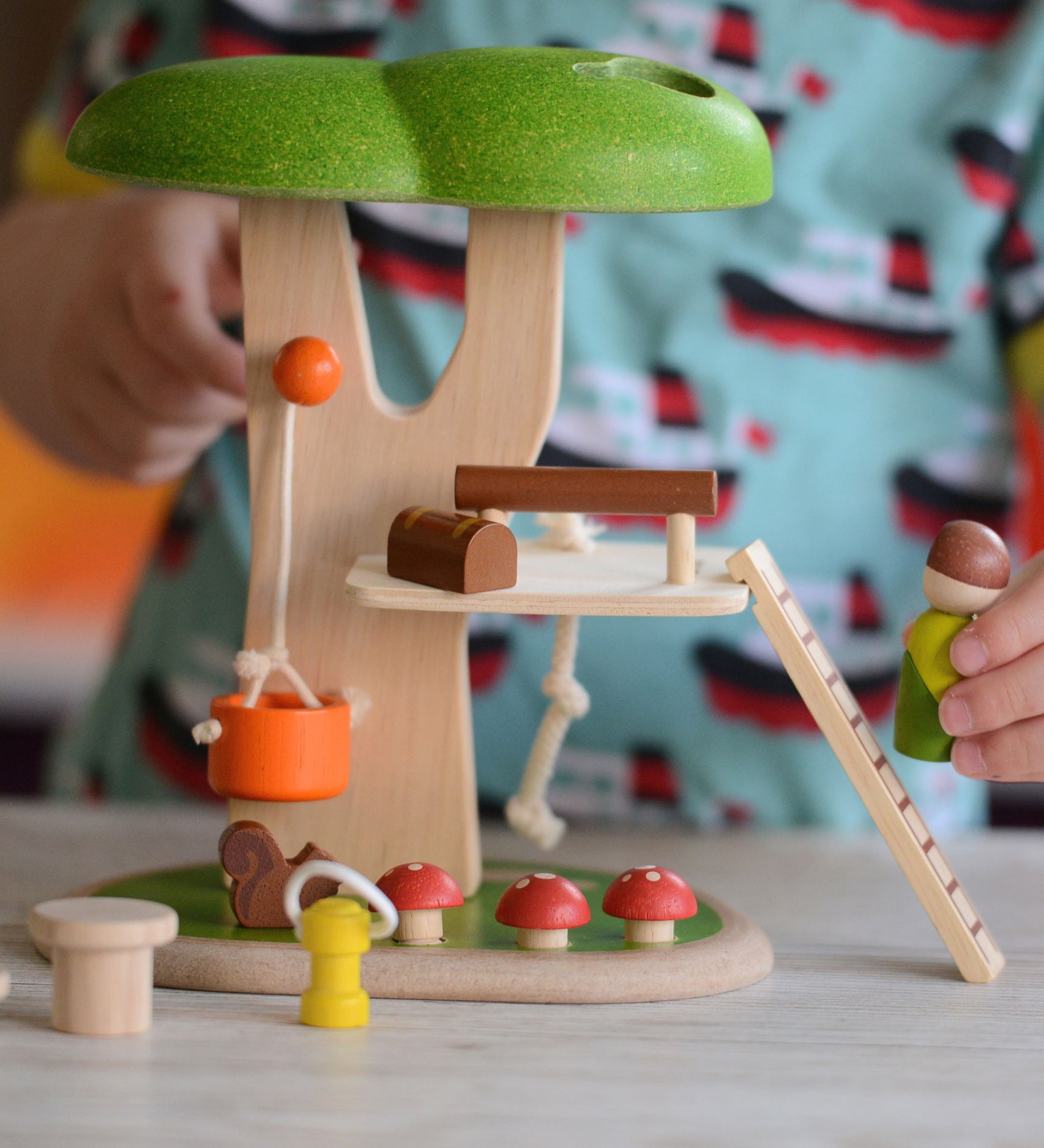 A close up of the PlanToys PlanWorld Tree House being played with by a child. The child's hand can be seen holding onto the little wooden doll figure. 