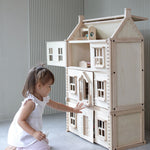 A child sitting in front of a PlanToys Victorian Dolls House with the basement attached. 