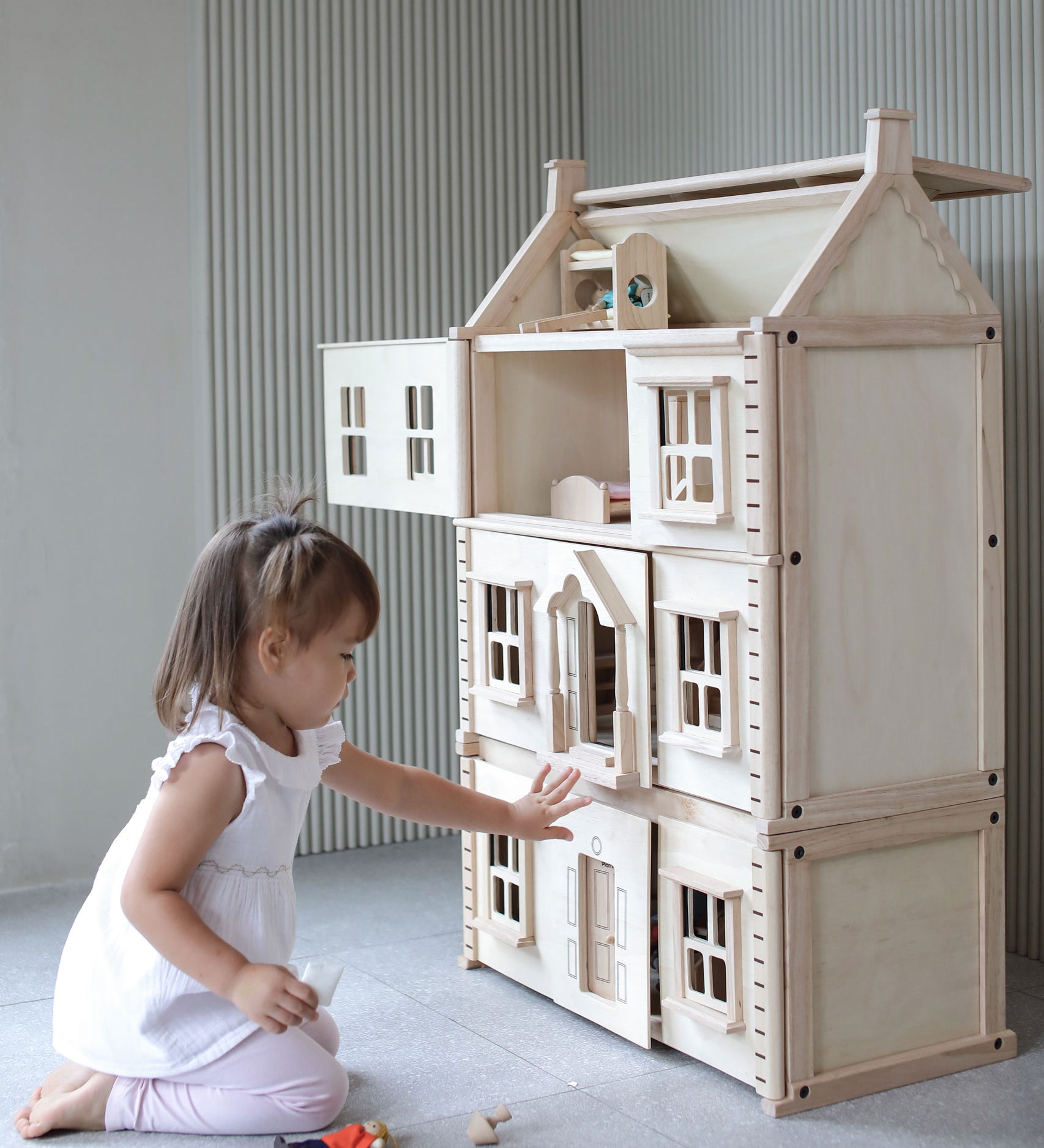 A child sitting in front of a PlanToys Victorian Dolls House with the basement attached. 