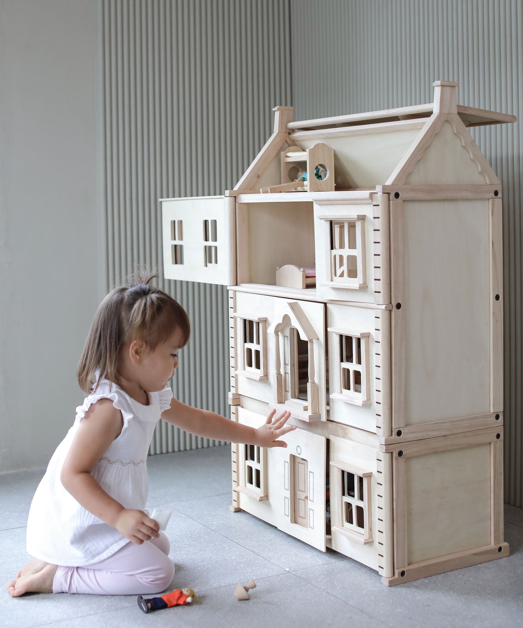 A child sitting in front of a PlanToys Victorian Dolls House with the basement attached. 