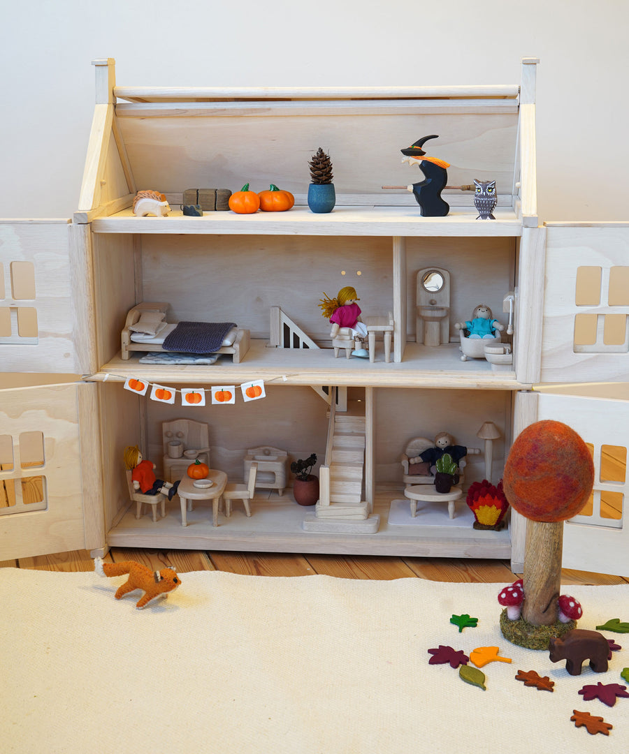 A PlanToys Victorian dolls house with furniture inside, decorated for Halloween, with paper pumpkin bunting made with the Babipur Pumpkin tape. 
