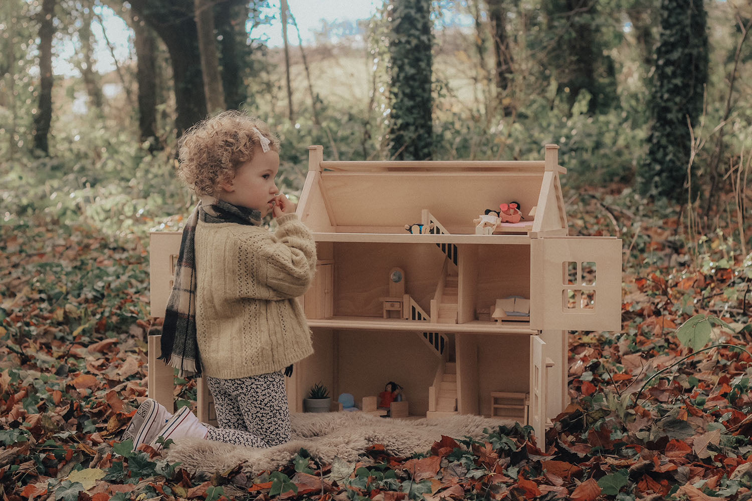 A child playing with the PlanToys Victorian Dolls House in a forest. 
