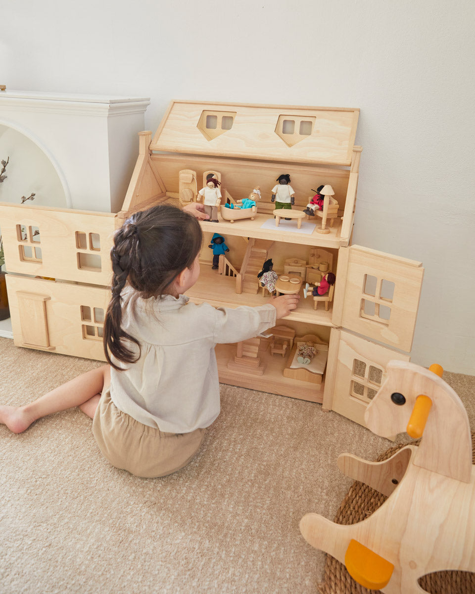 Girl sat on the floor next to the PlanToys Victorian dollhouse