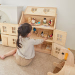 Girl sat on the floor next to the PlanToys Victorian dollhouse