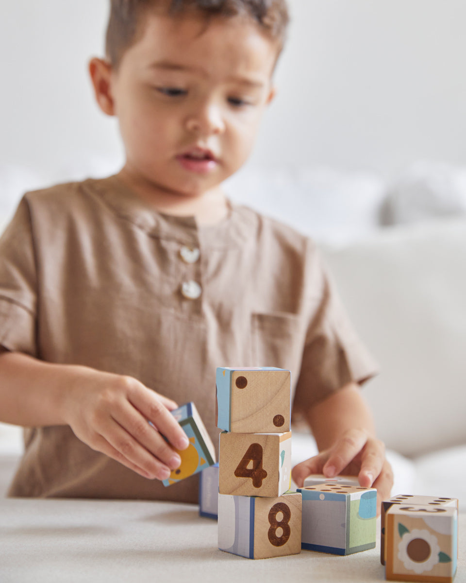 Young boy ordering the numbers on the back of the PlanToys plastic-free animal puzzle blocks on a beige sofa