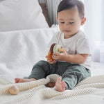 Young boy sat on a white bed playing with the PlanToys wooden stacking rings Waldorf toy