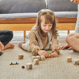 Young girl laying on the floor playing with the small wooden dog figure from the PlanToys plastic-free storytelling dice set