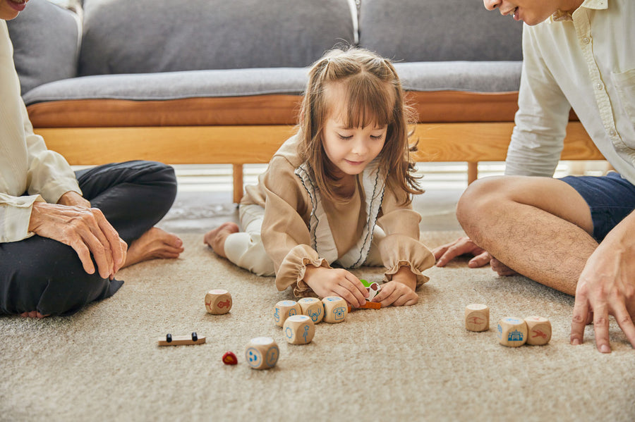 Young girl laying on the floor playing with the small wooden dog figure from the PlanToys plastic-free storytelling dice set