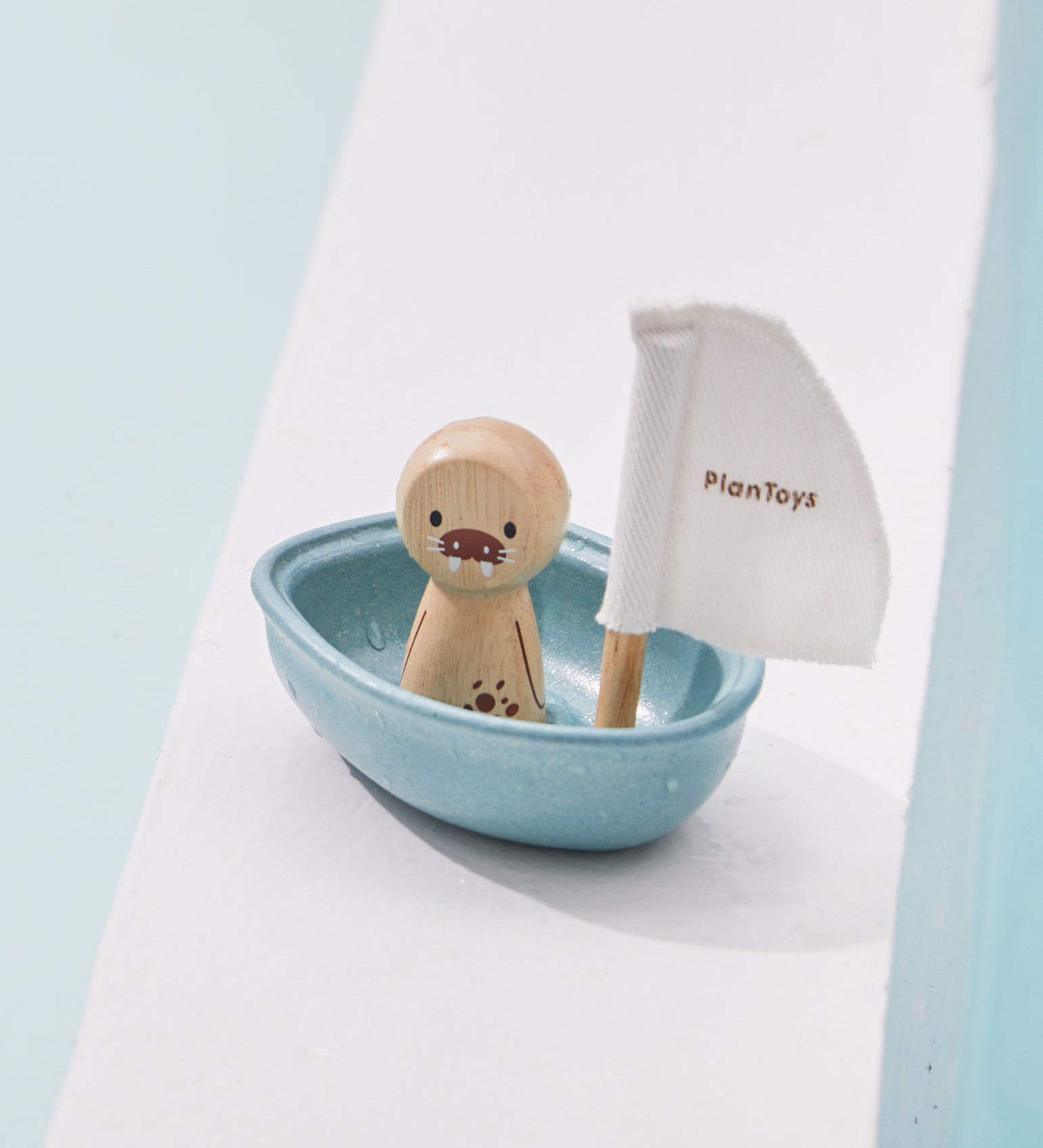 A PlanToys Walrus Sailing Boat toy placed on the side of a pool. 
