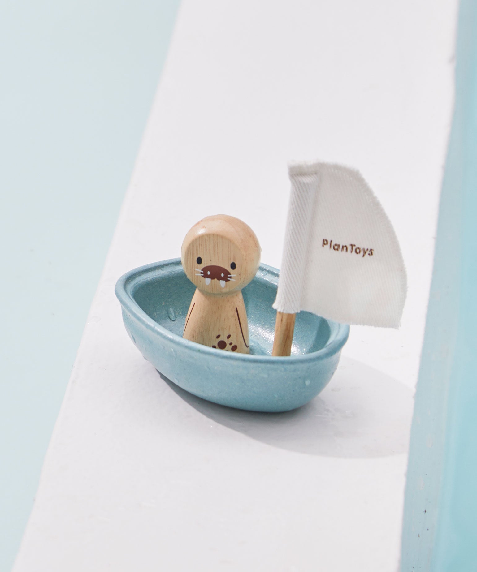 A PlanToys Walrus Sailing Boat toy placed on the side of a pool. 
