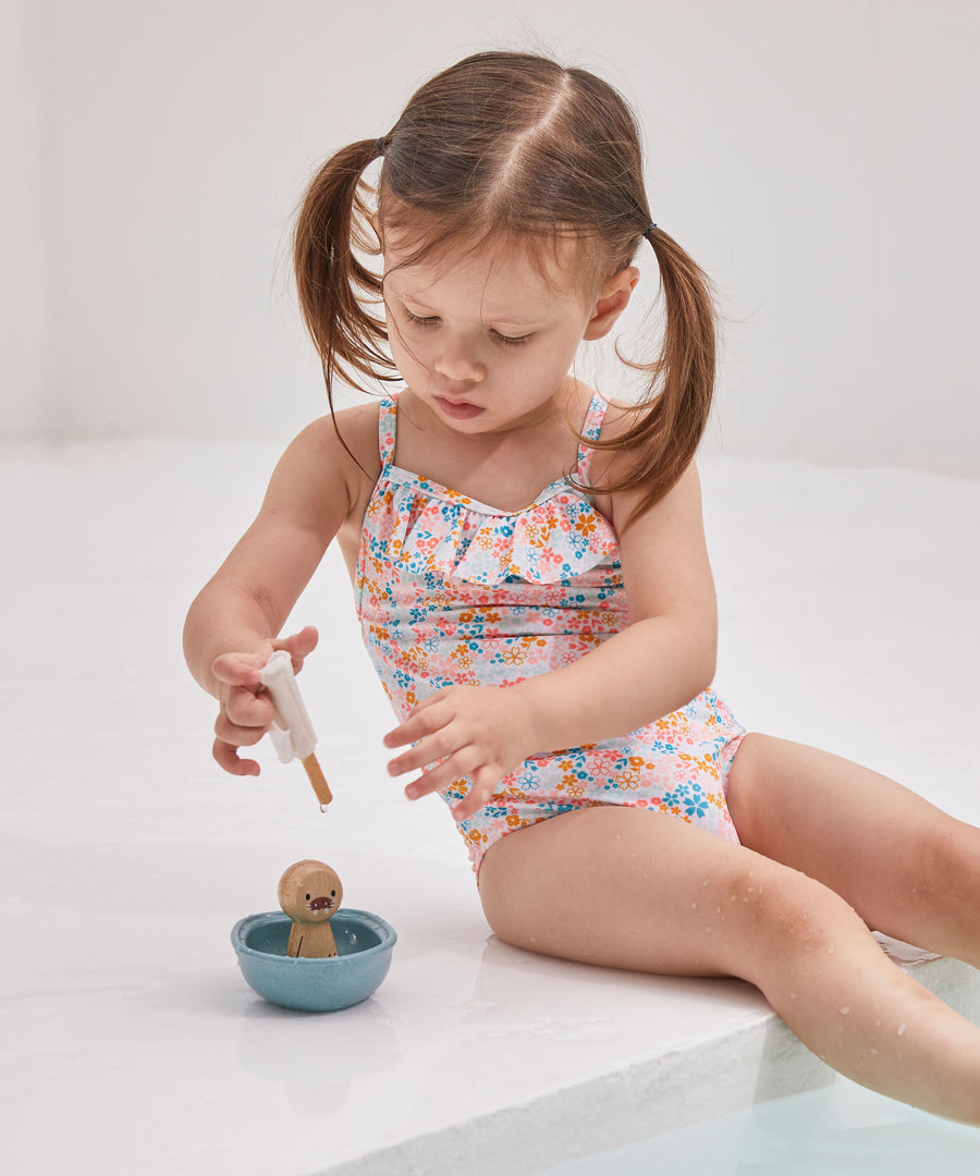 A girl sat on the edge of a swimming pool playing with the PlanToys wooden walrus sailing boat water toy. 