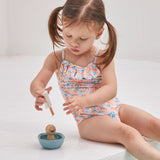 A girl sat on the edge of a swimming pool playing with the PlanToys wooden walrus sailing boat water toy. 