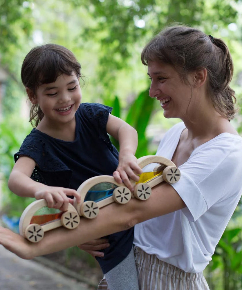 A child playing with the PlanToys Water Block Cars, the child is placing them on an adult's arm. 
