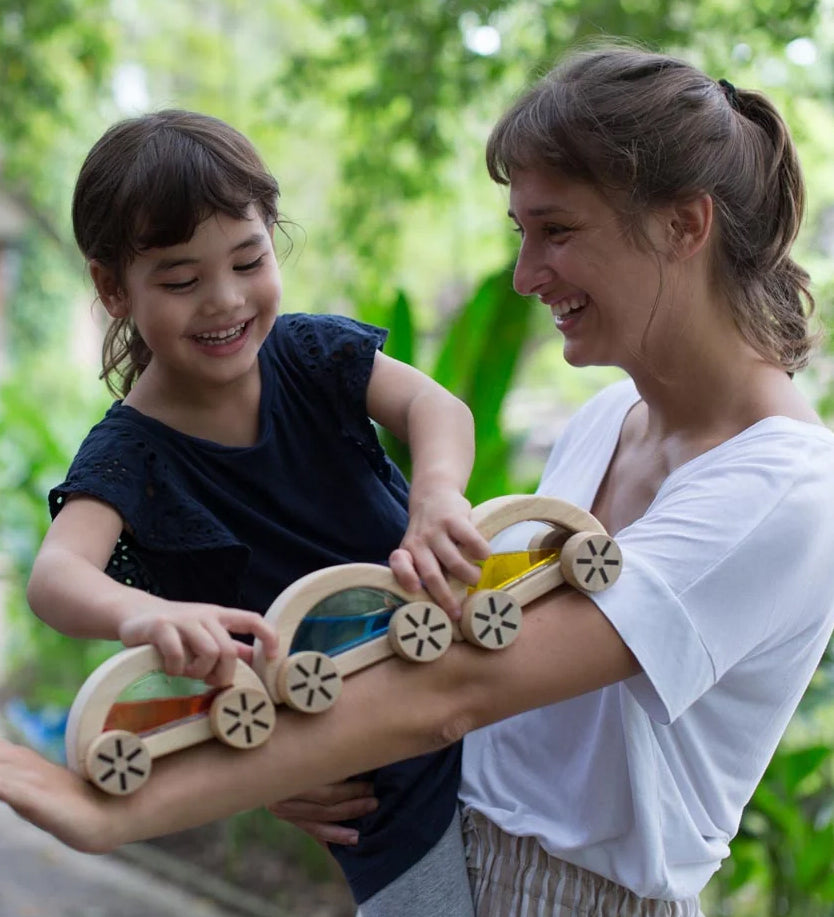 A child playing with the PlanToys Water Block Cars, the child is placing them on an adult's arm. 
