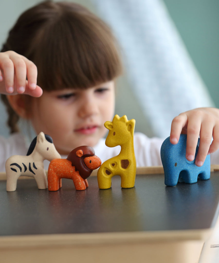 A child playing with the PlanToys Wild Animals Set, she has her hand on the blue coloured elephant figure. 