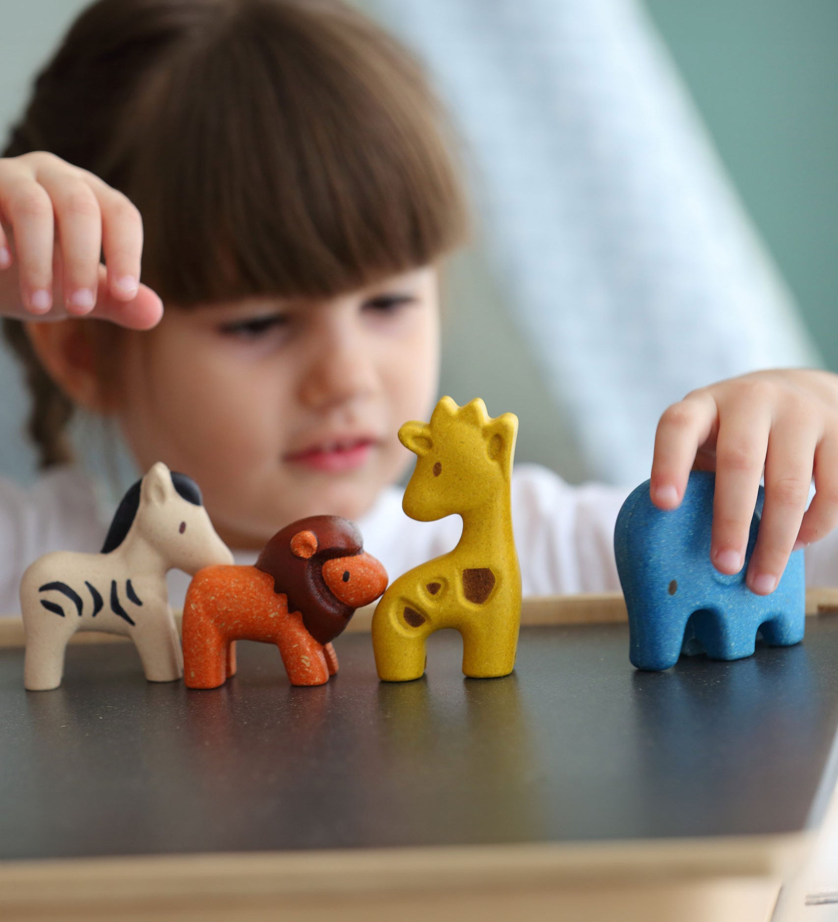 A child playing with the PlanToys Wild Animals Set, she has her hand on the blue coloured elephant figure. 