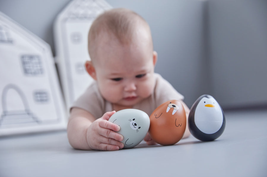 Close up of baby laying on a grey floor reaching for the PlanToys woobly seal