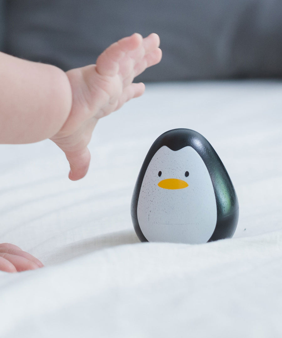 A baby's hand reaching for the PlanToys wobbly wooden penguin toy. 