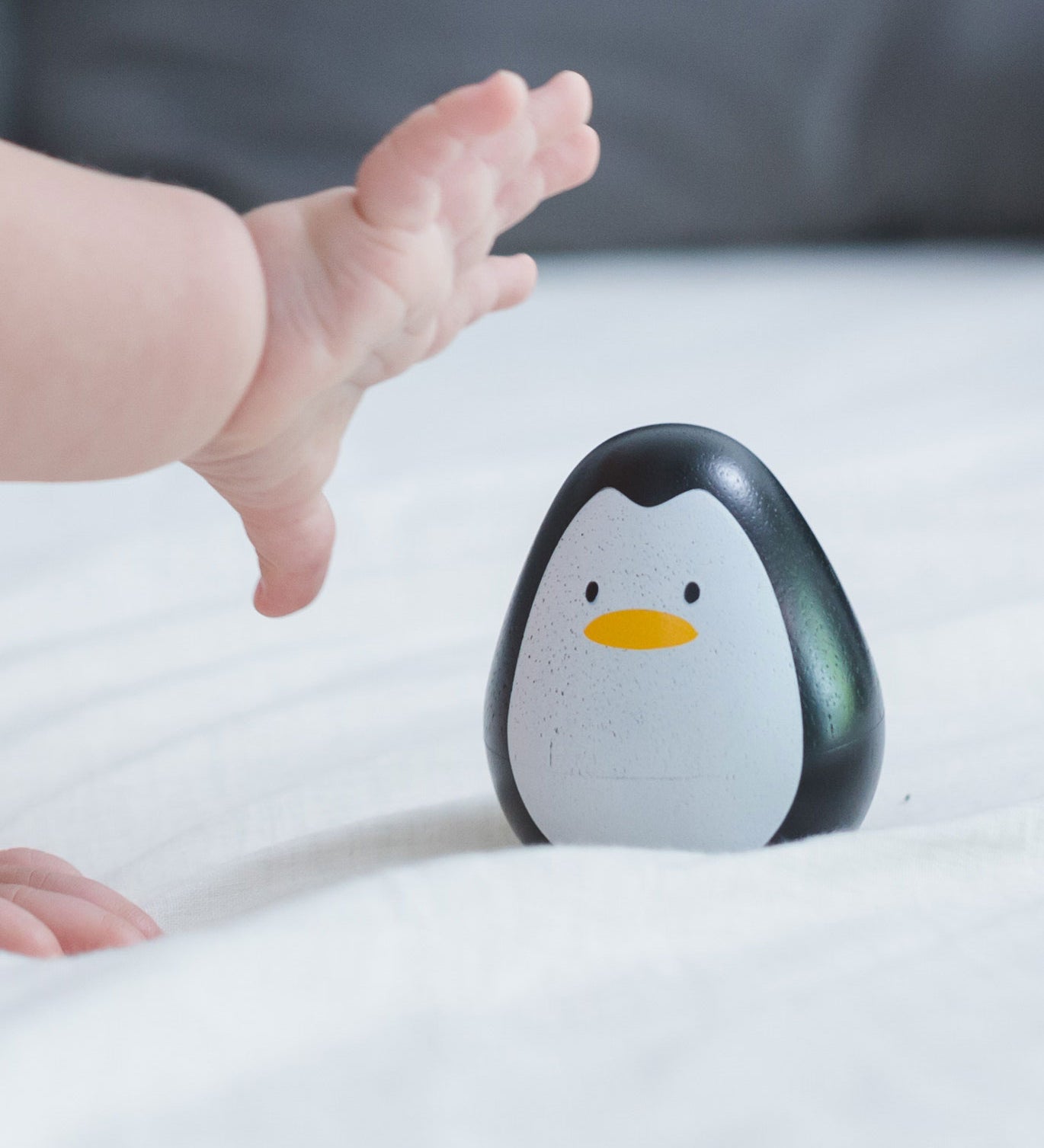 A baby's hand reaching for the PlanToys wobbly wooden penguin toy. 